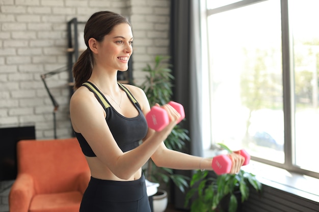 Junges schönes Sportmädchen in Leggings und einem Top macht Übungen mit Hanteln. Gesunder Lebensstil. Eine Frau treibt zu Hause Sport.