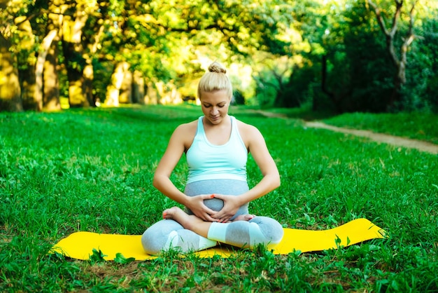 Junges schwangeres Mädchen, das Yoga im Park tut