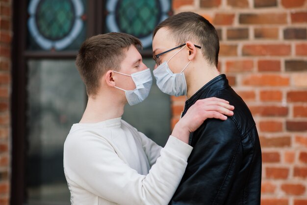 Junges schwules Paar, das medizinische Maske trägt, die Stadt umarmt und küsst