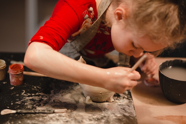 Junges siebenjähriges Mädchen in der Töpferei, das eine Schüssel aus Ton herstellt. Töpferwerkstatt für Kinder.