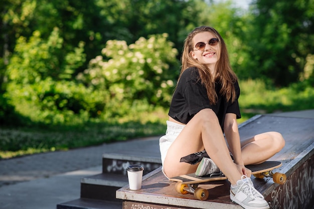 Junges Skatermädchen, das sich mit einem Skateboard im Skaterpark ausruht