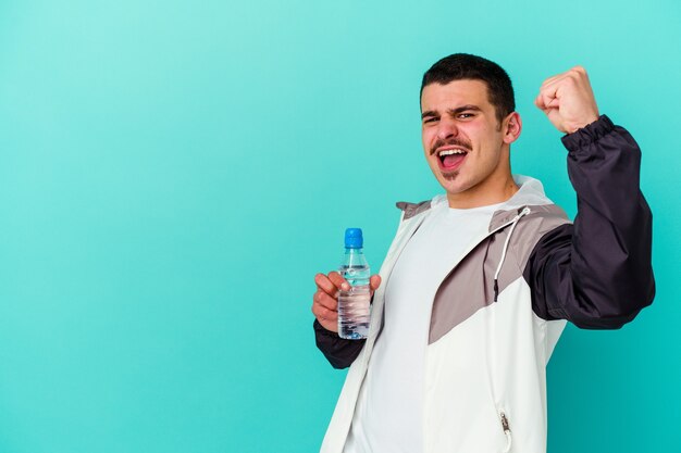 Junges sportliches kaukasisches Manntrinkwasser lokalisiert auf blauer erhebender Faust nach einem Sieg, Gewinnerkonzept.