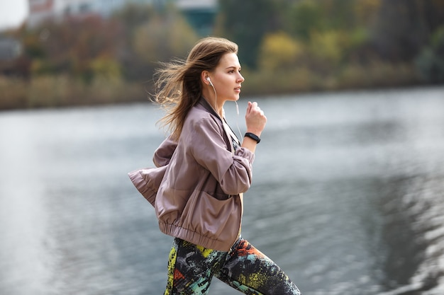 Junges sportliches Mädchen, das am Herbsttag im Stadtpark joggt.