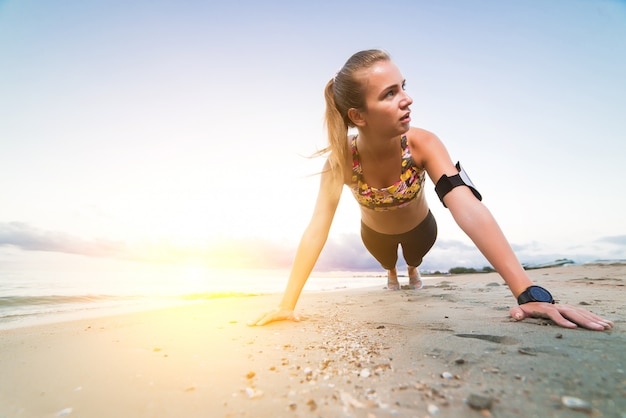 Junges sportliches Mädchen, das Plankenübung auf Strand bei Sonnenaufgang tut