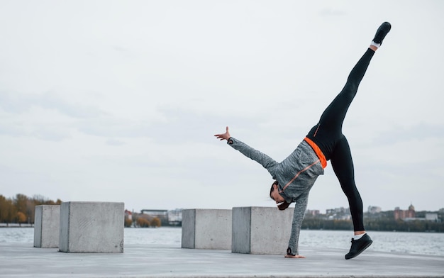 Junges sportliches Mädchen, das tagsüber Parkour-Stunts im Freien in der Nähe des Sees macht