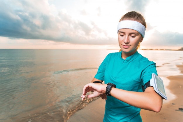 Junges sportliches mädchen, das uhr auf strandsonnenaufgang betrachtet