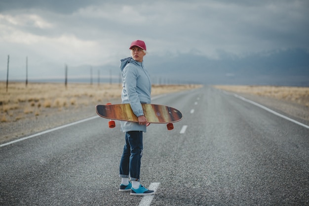 Junges sportliches Mädchen mit Longboard steht auf einer verlassenen Straße