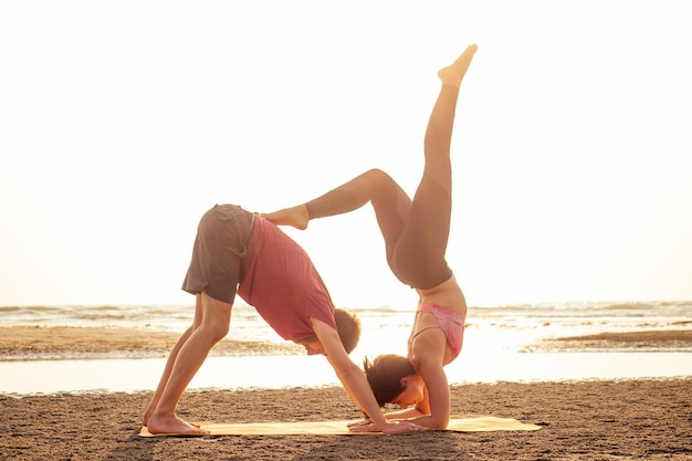 Junges sportliches Paar Mädchen und Junge üben Acroyoga-Übungen im Sonnenuntergang am Strand.