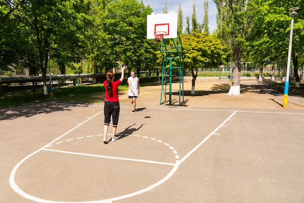 Junges sportliches Paar zusammen Basketball spielen - Frau erschossen auf Outdoor-Platz im üppigen grünen Park