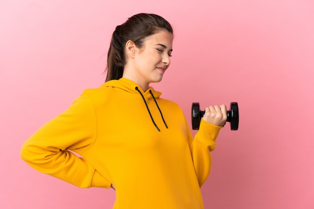 Junges Sportmädchen, das Gewichtheben über isoliertem rosa Hintergrund macht, der unter Rückenschmerzen leidet, weil es sich bemüht hat