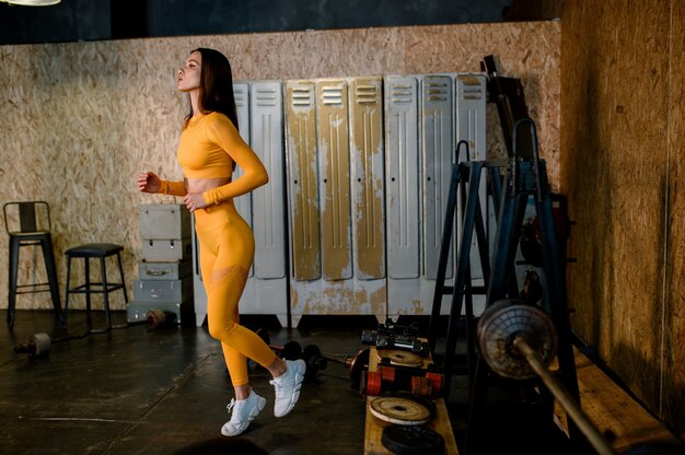 Junges Sportmädchen in einer gelben Sportuniform machen Sie sich bereit für ein Training im modernen Loftstyle-Fitnessstudio
