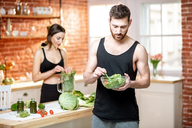 Junges Sportpaar mit Snack mit gesundem Salat und grünem Smoothie in der Küche zu Hause