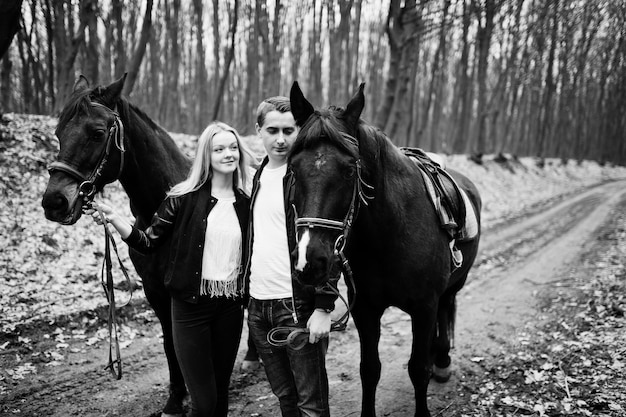 Junges stilvolles verliebtes Paar in der Nähe von Pferden im Herbstwald Schwarz-Weiß-Foto