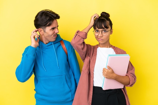 Junges Studentenpaar isoliert auf gelbem Hintergrund, das Zweifel hat, während es sich am Kopf kratzt