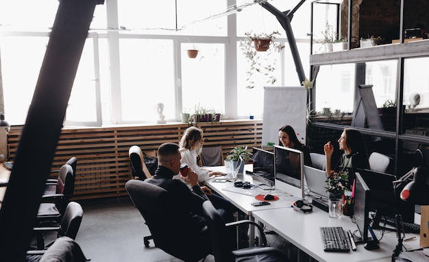 Junges Team arbeitet in einem geräumigen, hellen, modernen Open Space-Büro an einem Schreibtisch mit einem Computer und Laptops laptop