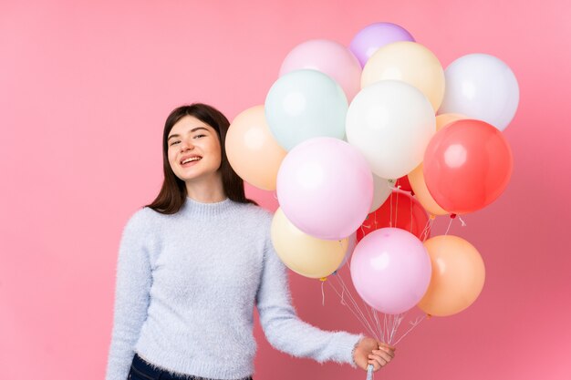 Junges Teenager-Mädchen, das viele Luftballons über rosa Wand lachend hält