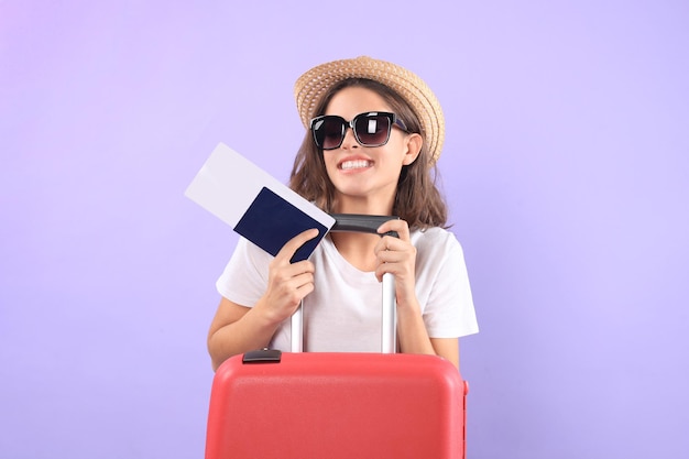 Junges Touristenmädchen in sommerlicher Freizeitkleidung, mit Sonnenbrille, rotem Koffer, Reisepass einzeln auf violettem Hintergrund