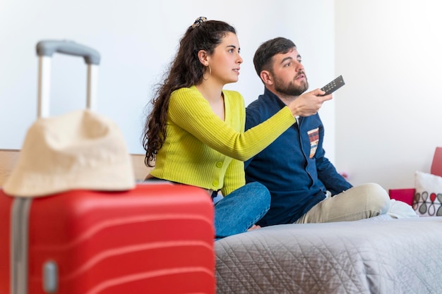 Junges Touristenpaar, das in einem Hotelzimmer auf dem Bett sitzt und fernsieht