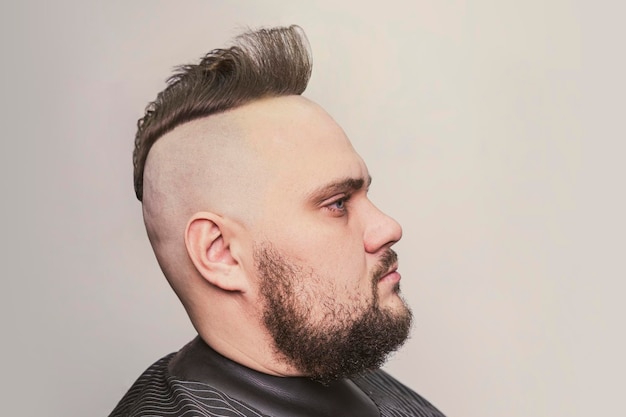 Junges trendiges Mannporträt Mann im Punk-Stil mit Mohawk-Frisur auf grauem Hintergrund