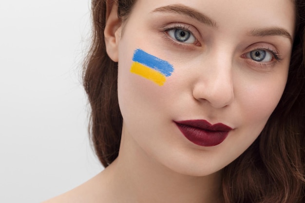Junges ukrainisches Mädchen mit weinrotem Lippenstift auf den Lippen, langes Haar, Nahaufnahme, Gelbblau auf den Wangen. Beten Sie für die Ukraine
