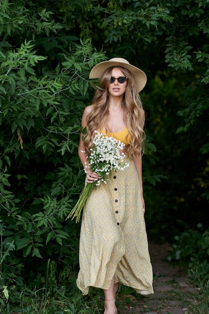 junges umwerfendes Mädchen in einem Sommeroutfit und mit weißen Blumen in den Händen im Wald