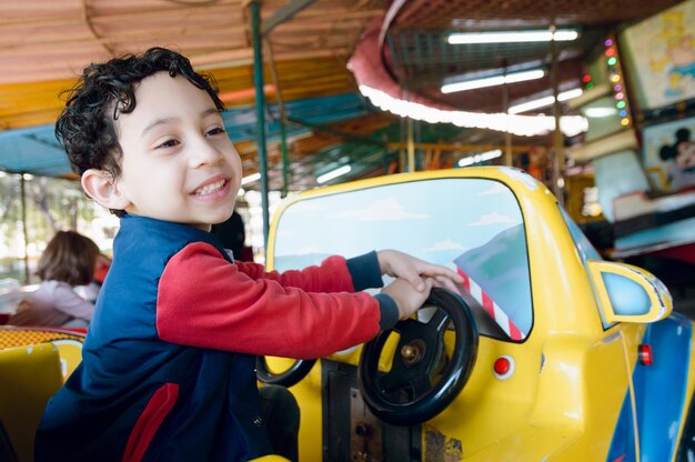 Junges venezolanisches lateinamerikanisches Kind, das glücklich lächelt und beim Fahren eines Elektroautos auf der Karussellmesse spielt