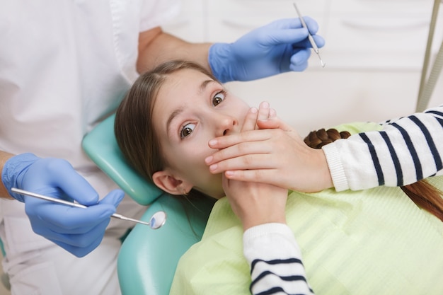 Junges verängstigtes Mädchen, das ihren Mund bedeckt, der Zahnuntersuchung durch Zahnarzt ablehnt