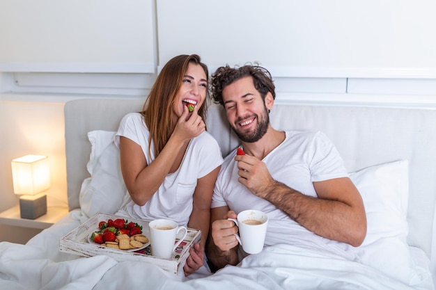 Junges verliebtes Ehepaar, das in ihrem Bett frühstückt. Guten Morgen! Gesundes Frühstück im Bett. Junges schönes Liebespaar frühstückt im Bett.