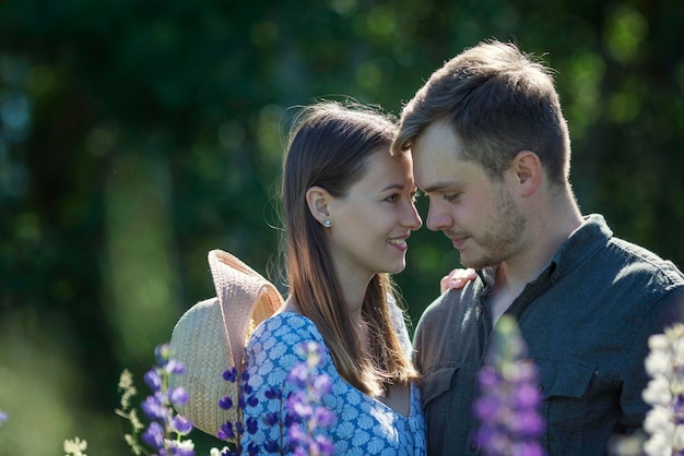 Junges verliebtes Paar lächelt und umarmt in der Natur in Blumen Schöner Park mit blühenden lila Lupinen Liebe und Zärtlichkeit