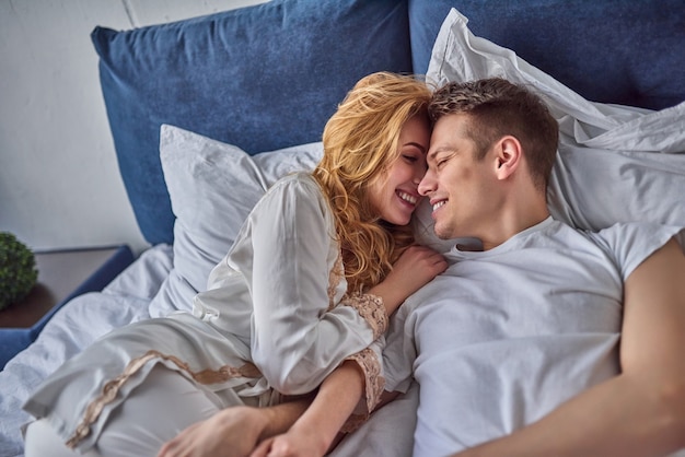 Foto junges verliebtes paar liegt im bett, lächelt und albert herum.