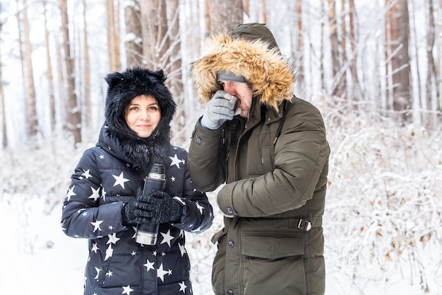 Junges verliebtes Paar trinkt ein heißes Getränk aus einer Thermoskanne und genießt die Winternatur.