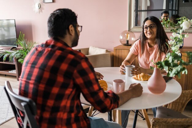 Junges, vielfältiges Liebespaar, das Croissants isst und zu Hause in der Frühstückszeit miteinander spricht Kommunikations- und Beziehungskonzept