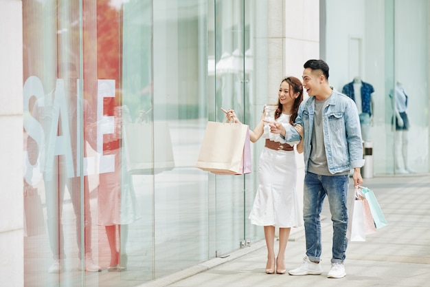 Junges vietnamesisches Paar, das in der Woche im Einkaufszentrum einkauft, geht und durch Schaufenster schaut