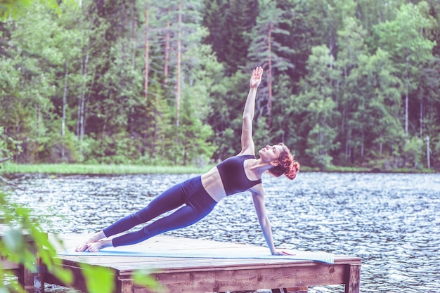 Junges Yogi-Mädchen, das Yoga praktiziert Side Plank-Übung Vasisthasana-Pose auf dem See Das Konzept der Beschwichtigung eines gesunden Lebensstils