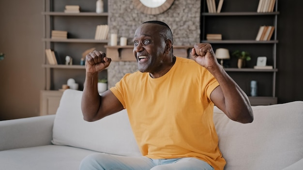 Junggeselle eines älteren fußballfans, afroamerikaner, sitzt auf einem gemütlichen sofa in einer wohnung und sieht tv-sport