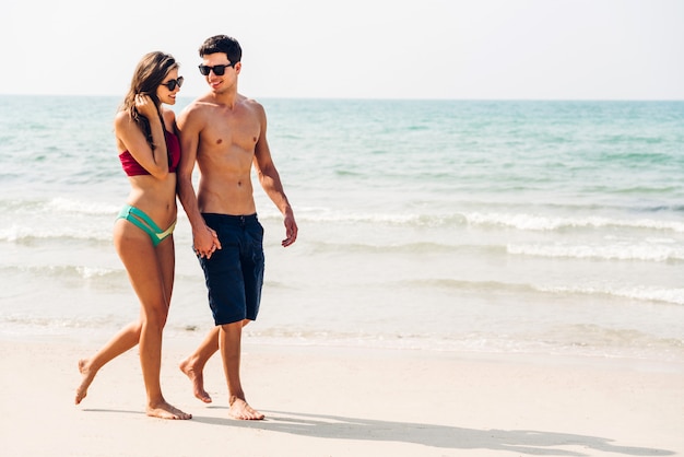 Jungpaar des romantischen Liebhabers, das Hände hält, die zusammen auf dem tropischen Strand entspannend gehen. Sommerferien