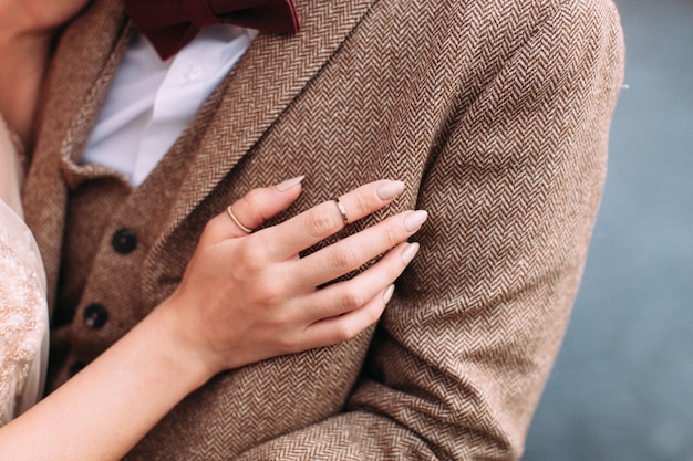 Jungvermählten Braut legte ihre Hand mit goldenen Ringen auf die Brust ihres Bräutigams In Tweedjacke. Konzept der Familie, Liebe, Hochzeitstag