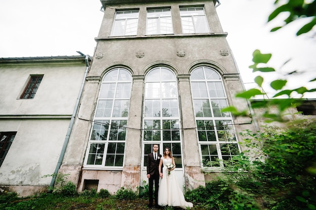 Jungvermählten stehen in einem botanischen Garten in der Nähe der alten Architektur und schauen auf die Kamera. Hochzeitszeremonie im Park.