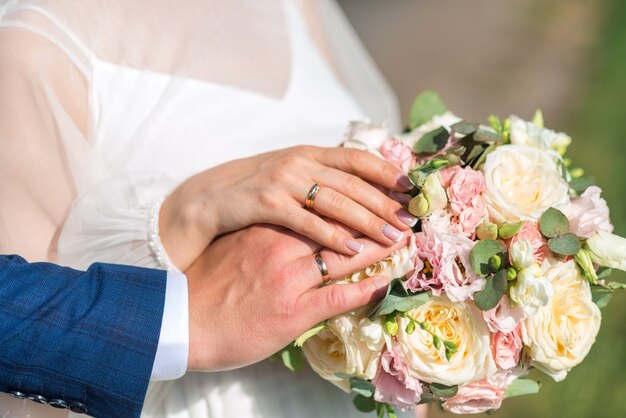 Jungvermähltenhände mit Ringen. Hochzeitsstrauß auf dem Hintergrund der Hände der Braut und des Bräutigams mit einem goldenen Ring