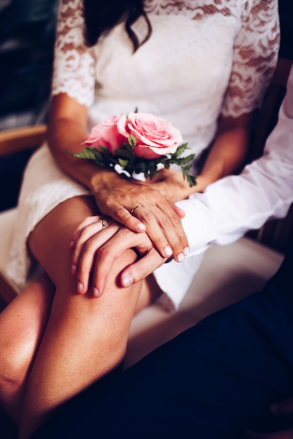 Jungvermähltenpaar mit ihren Eheringen und Rosenstrauß, die an ihrem Hochzeitstag streicheln. Braut und Bräutigam zeigen ihre Hand mit den Ringen.