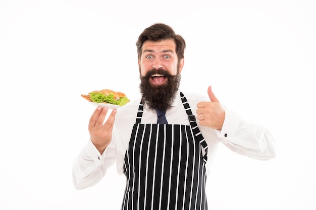 Junk-Food. Leckeres Croissant. Mann bärtiger Kellner tragen Schürze tragen Teller mit Essen. Café-Konzept. Kerl serviert Croissant gefüllt mit Salat und frischem Gemüse. Gesundes Essen. Kalorien und Diät.