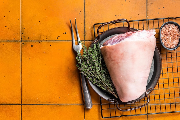 Junta de pernil de porco crua em uma bandeja de aço com ervas Fundo laranja Vista superior Copie o espaço