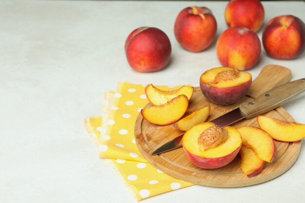 Junta con frutos de durazno, cuchillo y toalla de cocina en la mesa con textura blanca