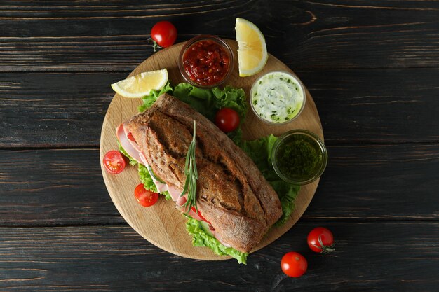 Junta con sándwich ciabatta e ingredientes en mesa de madera