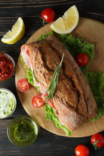 Junta con sándwich ciabatta e ingredientes en mesa de madera