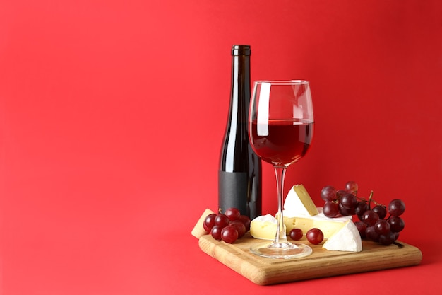 Junta con vino, queso y uva sobre fondo rojo.