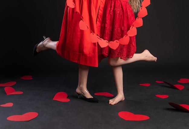 Juntas, madre e hija sostienen guirnaldas de corazones, símbolo rojo feliz, coqueteo de corazón en el suelo