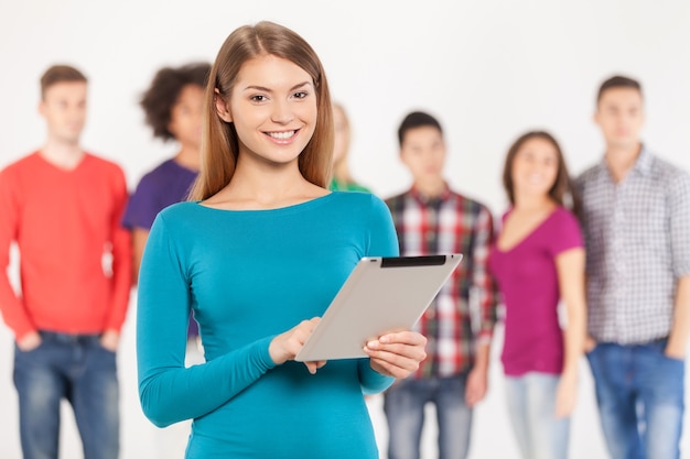 Junte-se a uma era digital. Jovem alegre segurando um tablet digital enquanto seus amigos estão de pé no fundo