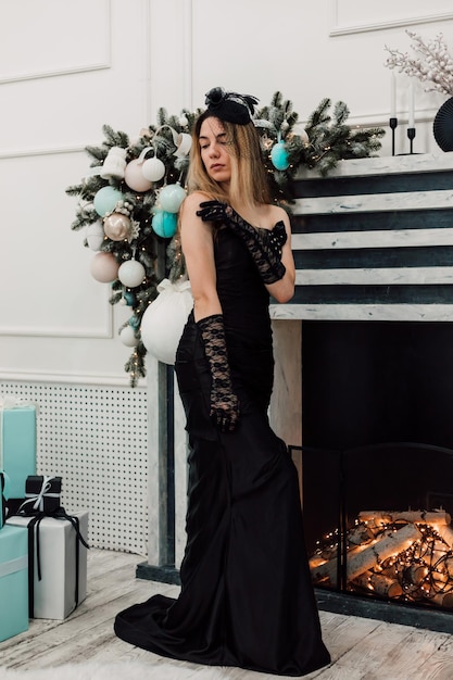 Junto à lareira de Ano Novo adornado jovem posando em um vestido preto longo
