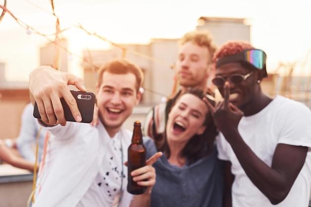 Juntos e tirando selfie Grupo de jovens em roupas casuais fazem uma festa no telhado juntos durante o dia
